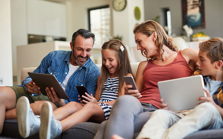 Family laughing together on couch using various devices