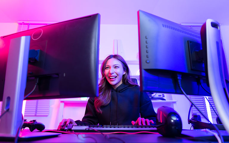 Young woman laughing at a computer desk with dual monitors