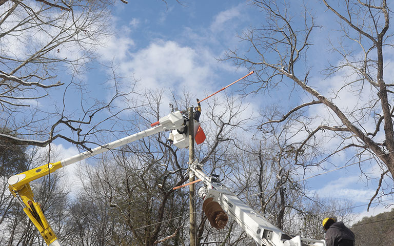 EPB Lineman working on powerpole around snow covered tree limbs