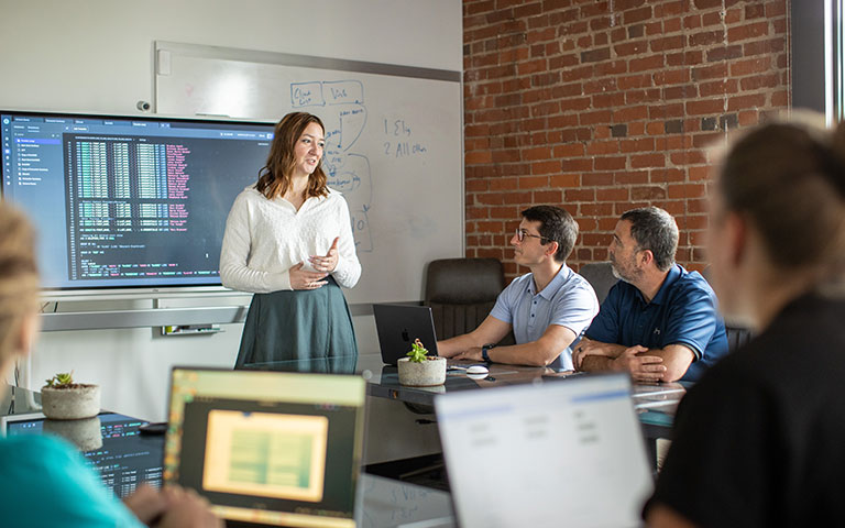EPB Employees sitting around a table while a woman is presenting in front of a projector